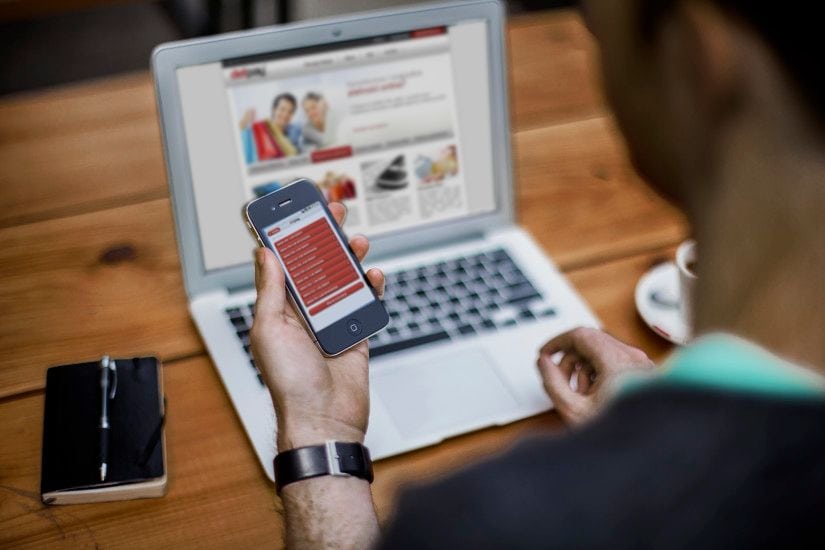 Biznes w sieci to szansa na odbudowę zysków - mężczyzna siedzi przy stole przed laptopem i trzyma telefon w ręku. 
