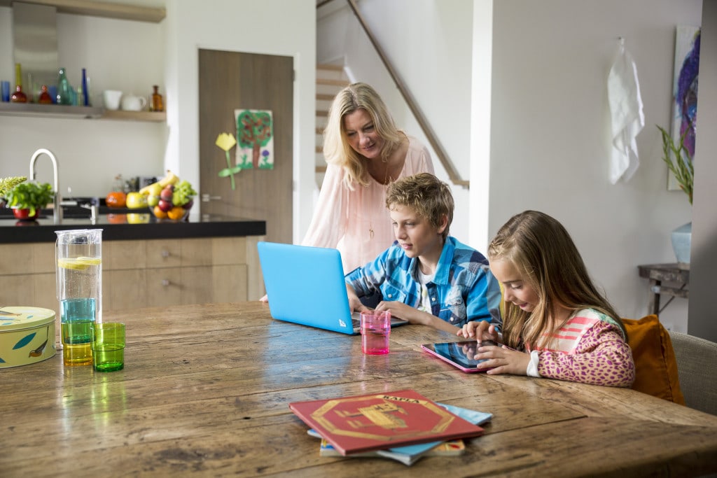 Od 1 lipca wyższe podatki dla samotnie wychowujących dzieci - kobieta patrzy na dwójkę dzieci, które siedzą przy stole i patrzą w laptop.a