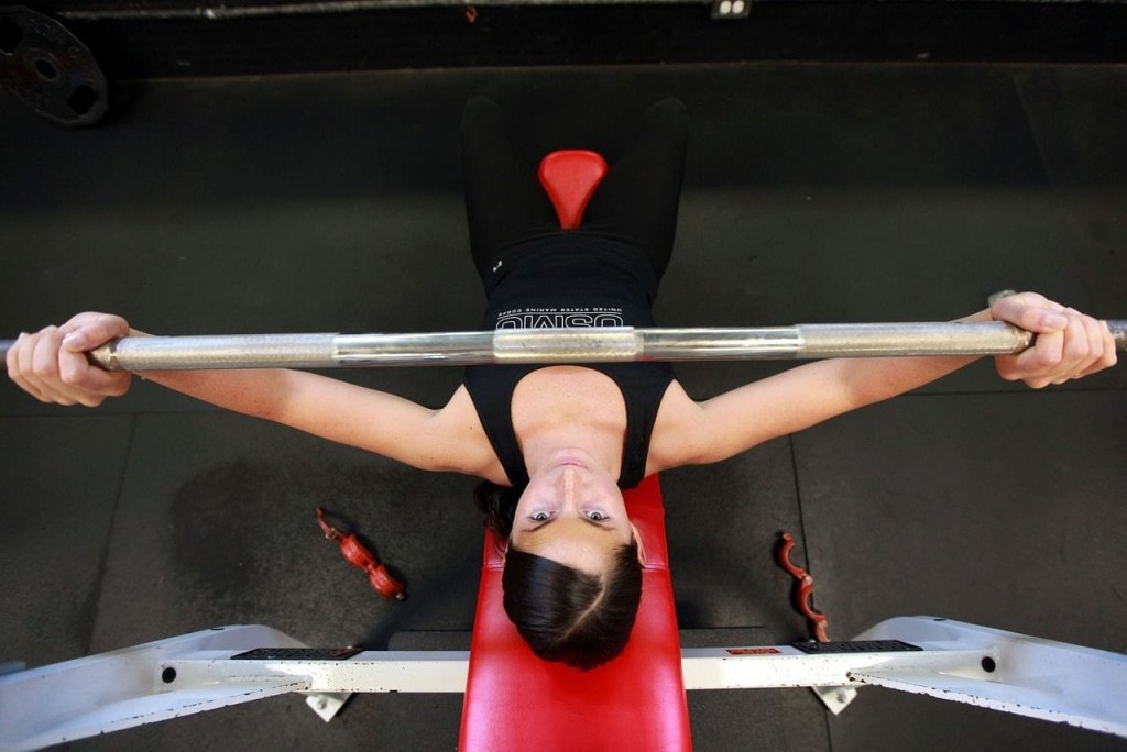 Czy branża fitness dostanie odszkodowania za straty z powodu lockdownu? - kobieta na siłowni leży na ławeczce i podnosi sztangę. 