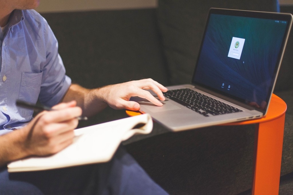 Edukacja biznesowa dla początkujących przedsiębiorców -mezczyzna siedzi na sofie i pisze w laptopie. 