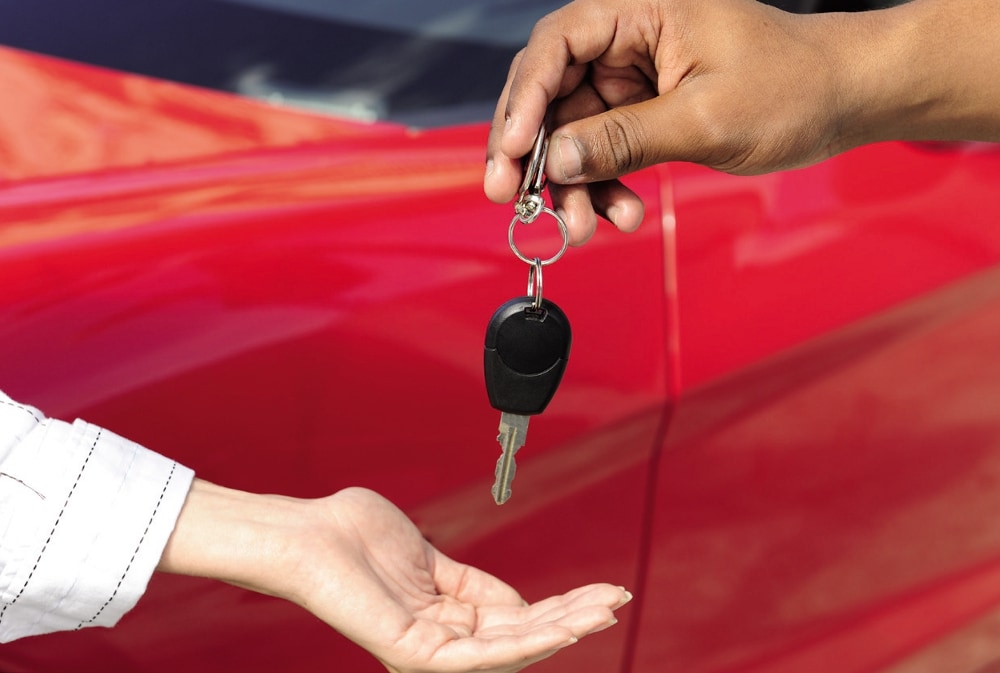 W epidemii rośnie liczba dłużników leasingowych- mężczyzna daje kobiecie klucze do ręki, w tle czerwone aut.