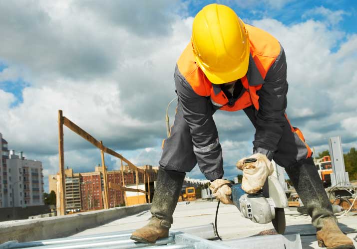 Cyfrowe zmiany w budownictwie obowiązujące od 1 stycznia 2023 r. - budowlaniec na dachu budynku tnie piłą metal. 