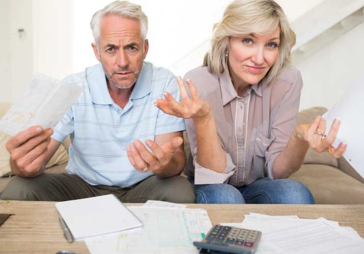 Domowe rachunki: mniej dłużników, większy dług - kobieta i mężczyzna siedzą przy  stole, na którym leżą rachunki. 