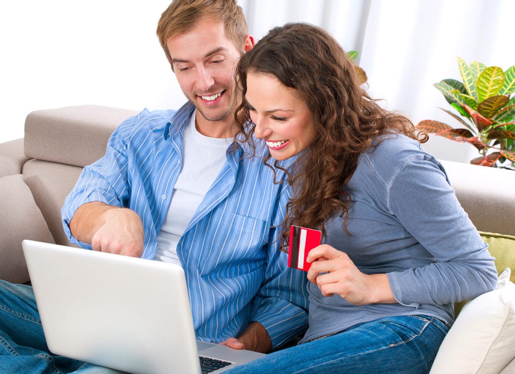 Zakupy online kosztują - czasem nie tylko pieniądze, ale i dane osobowe - kobieta i mężczyzna siedzą na kanapie przed otwartym laptopem z kartą płatniczą w ręku. 