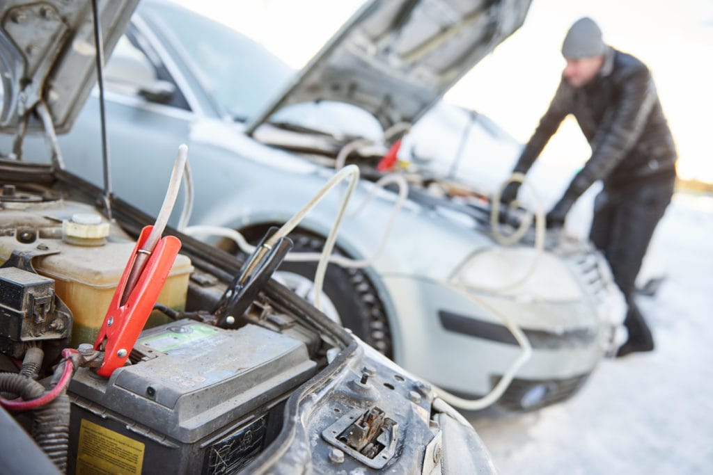 Najpopularniejsze szkody samochodów używanych i ich wartość - mężczyzna naprawia uszkodzone auto podłączone do drugiego samochodu.