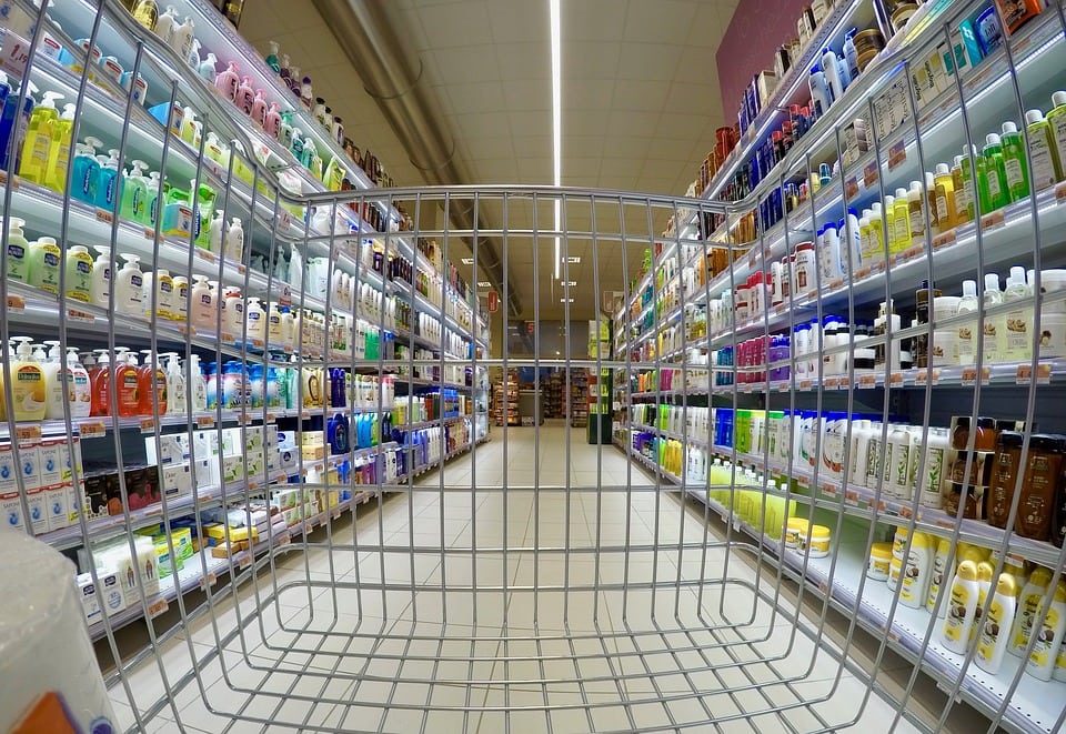 Żywność i paliwa napędzają inflację - wózek na zakupy stoi na środku sklepu pomiędzy półkami. 