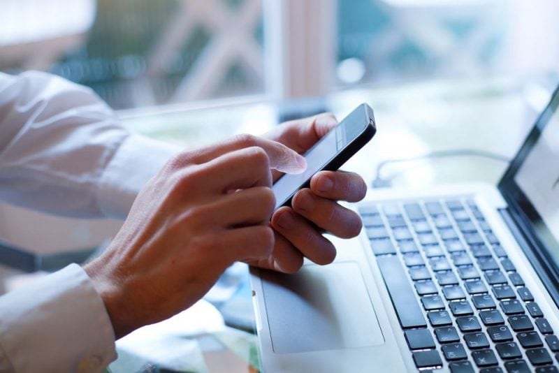 Sztuczna inteligencja wspiera klientów w zakupach online - mężczyzna siedzi przed laptopem, z telefonem w reku 