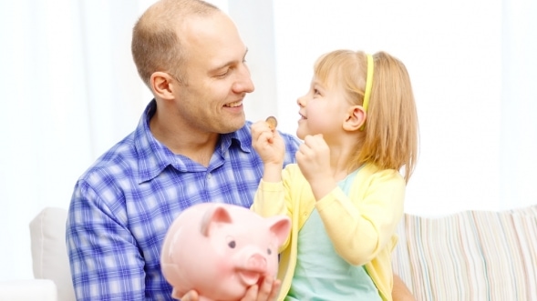 Jak zabezpieczyć finanse osobiste w dobie koronawirusa? Tata trzyma dziecko na kolanach i skarbonkę w ręce