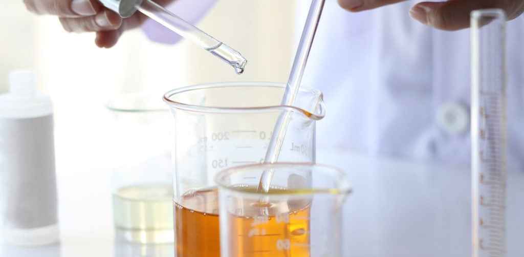 Testy genetyczne na koronawirusa już w produkcji- materiały szklane zwane kolbami, wraz z pipetami stoją na stole laboratoryjnym. 