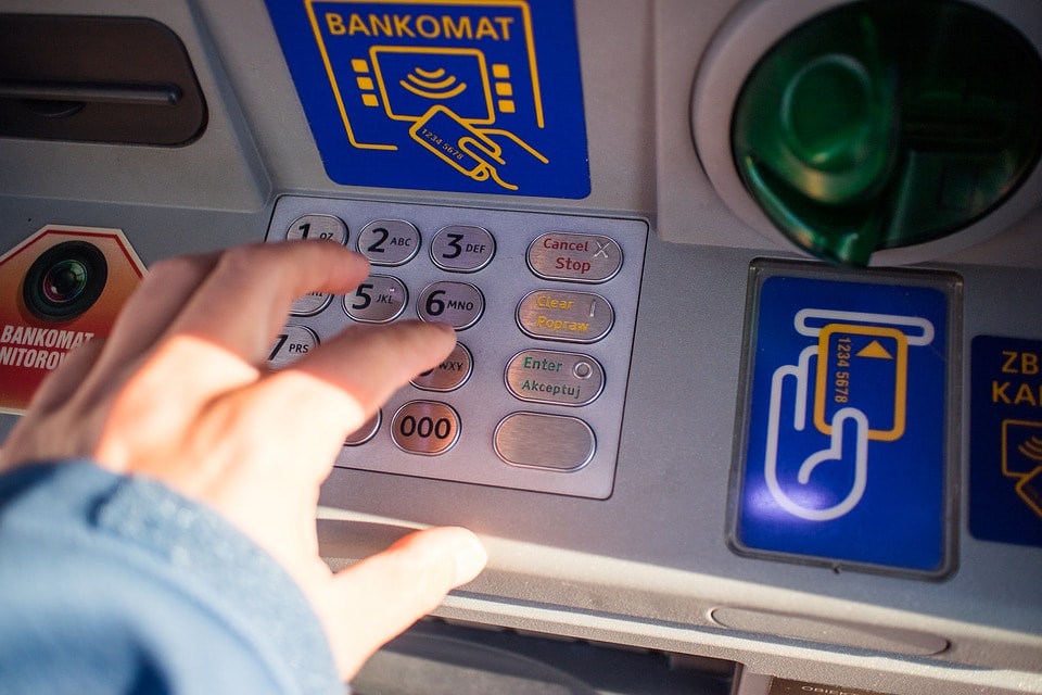 Ile płacimy za prowadzenie konta bankowego i dlaczego tak drogo? - męska dłoń wpisuje pin do bankomatu na klawiaturze urządzenia. . 