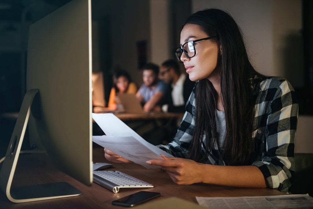 PIT na maila? Rekruterzy i działy HR coraz częściej działają online - kobieta siedzi prze ekranem komputera z dokumentami w ręku. 