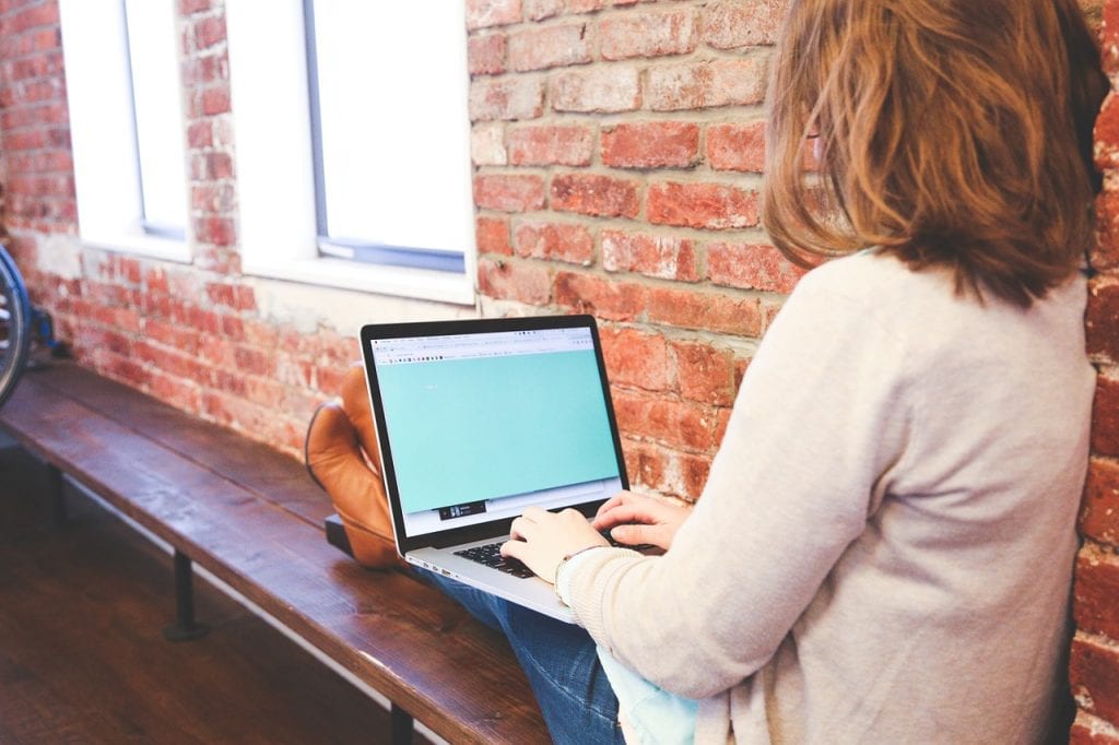 Sektor edukacji docenił zalety technologii cyfrowych - kobieta siedzi na ławce i pisze na klawiaturze laptopa.