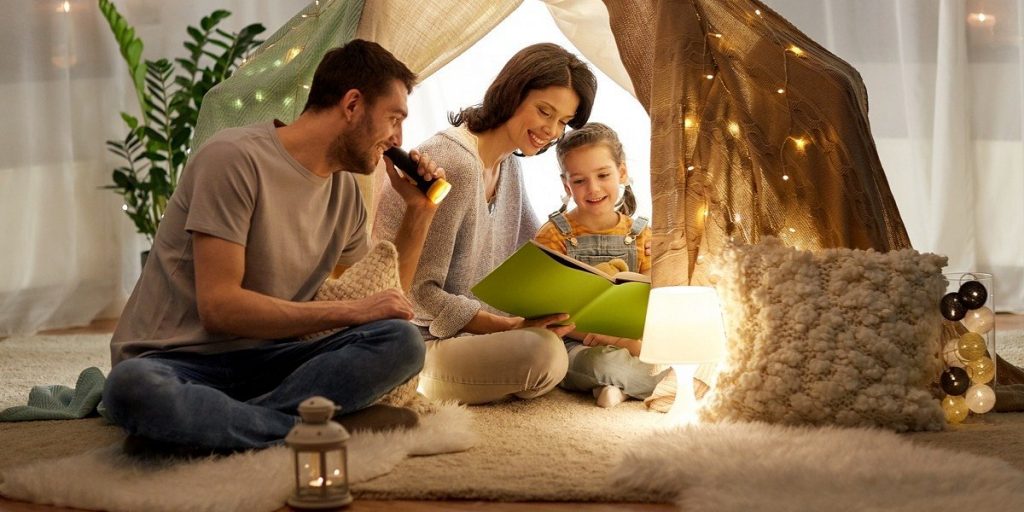 Najpopularniejsze książki października- kobieta, mężczyzna i dziecko siedzą na dywanie i czytają książkę