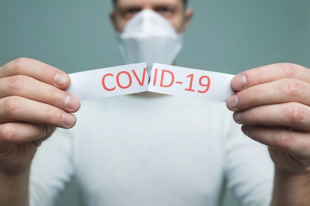 COVID-19: nowe obostrzenia i ulgi od 19 kwietnia - mężczyzna w masce na twarzy trzyma w ręku kartkę z napisem COVID-19.