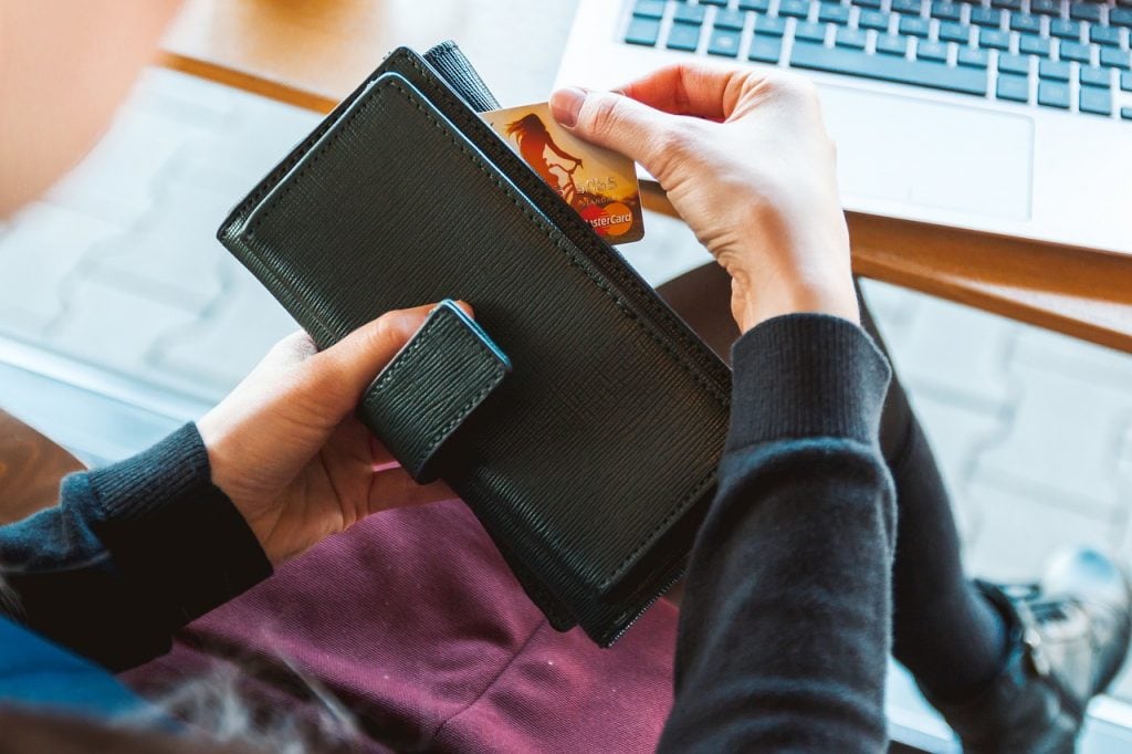 Rezerwacja usług online - dlaczego warto ją wprowadzić? - kobieta siędząca prze laptopem, wyciąga z portfela kartę kredytową