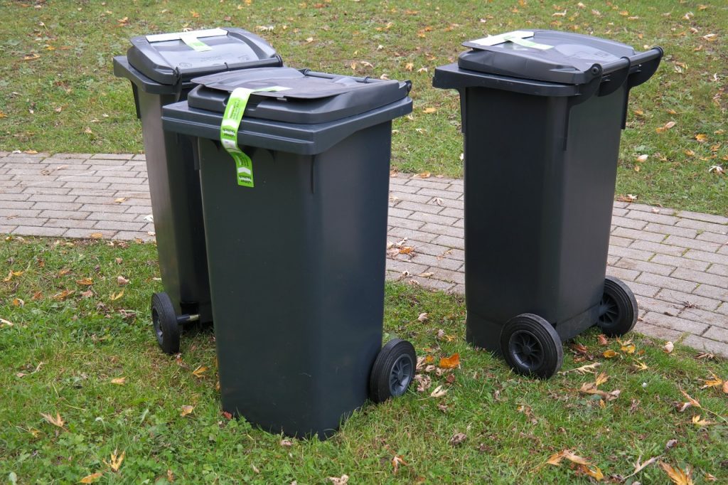 Gospodarowanie odpadami - kto za to powinien zapłacić? - trzy kosze na  śmieci stoją na trawie.