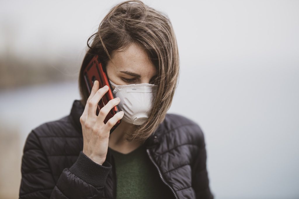 Nierealistyczny optymizm w pandemii- kobieta  z maseczką na twarzy rozmawia przez telefon. 