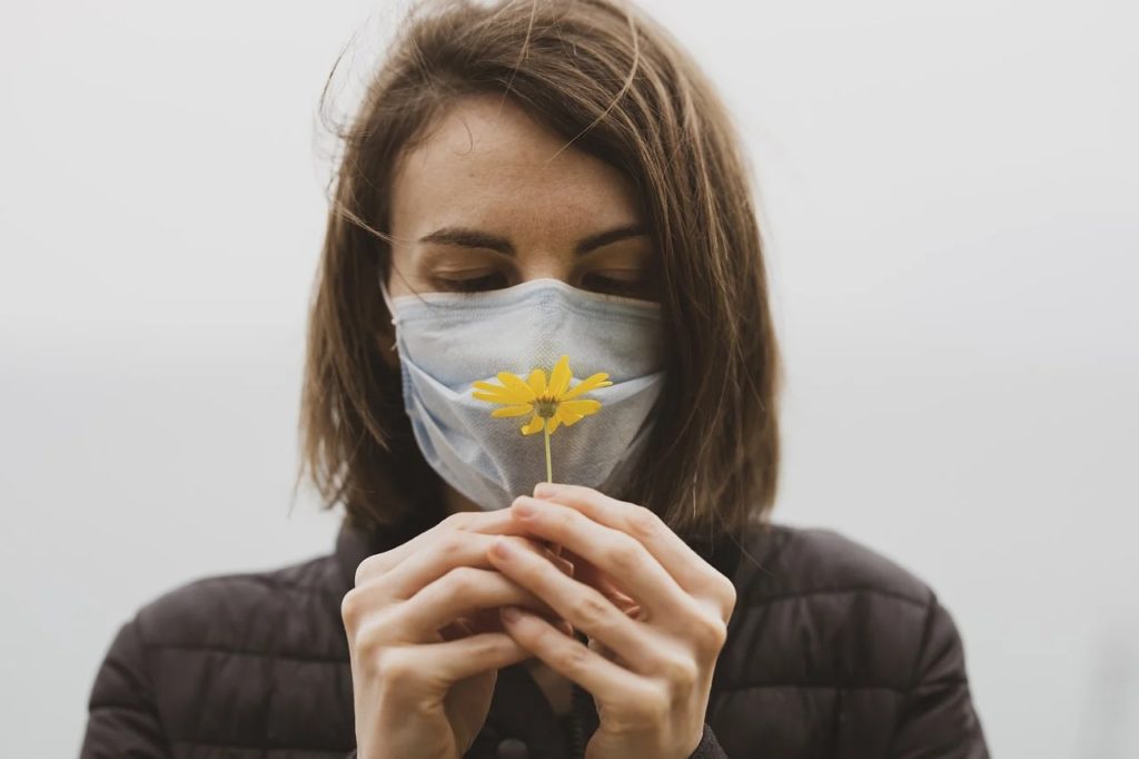 Solidarność Polaków w obliczu pandemii - kobieta z maseczką na twarzy trzyma w ręku żółtego  kwiatka.