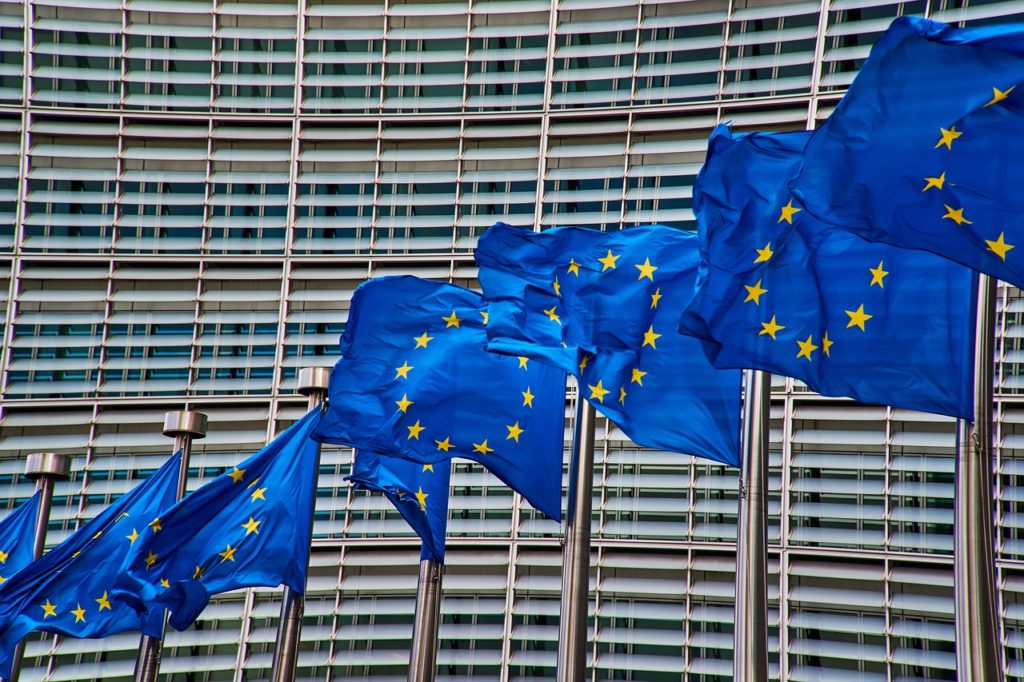 Baterie wielokrotnego ładowania - KE pracuje nad zmianami w prawie - flagi unii europejskiej w  tle budynku Komisji Europejskiej. 