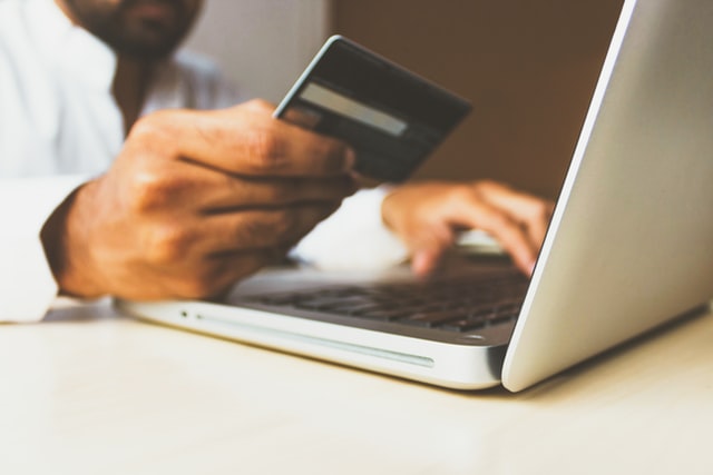 E-commerce rośnie jak nigdy wcześniej - mężczyzna siedzi przed otwartym laptopem z karta kredytowa w ręku. 