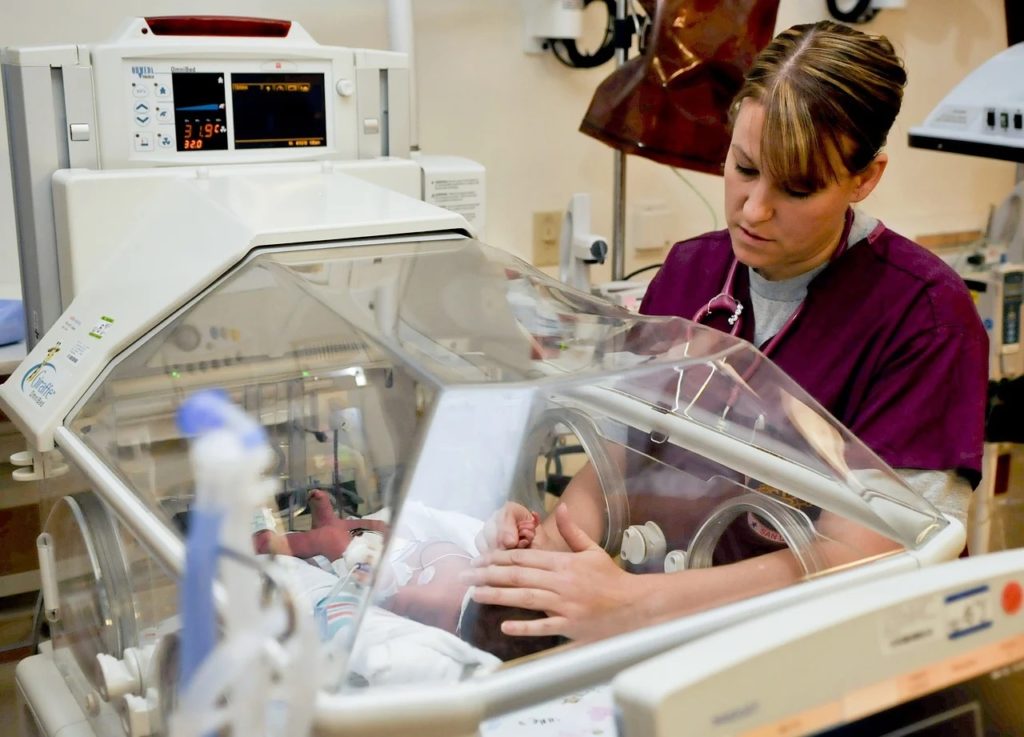 Brakuje specjalistów z fachem w ręku do pracy - położna bada noworodka  w inkubatorze. 