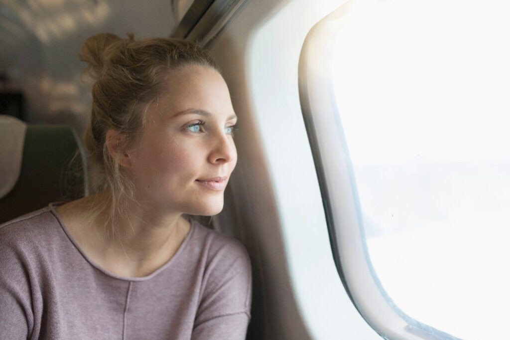 Żegnamy tryb samolotowy – nowa dyrektywa KE - kobieta siedzi przy oknie w samolocie i wygląda przez okno. 