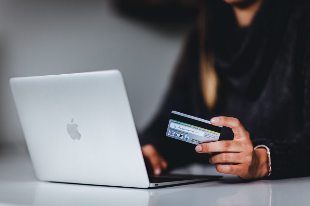 (Nie)bezpieczne zakupy w sieci -kobieta siedzi prze laptopem i trzyma w reku kartę kredytową. 