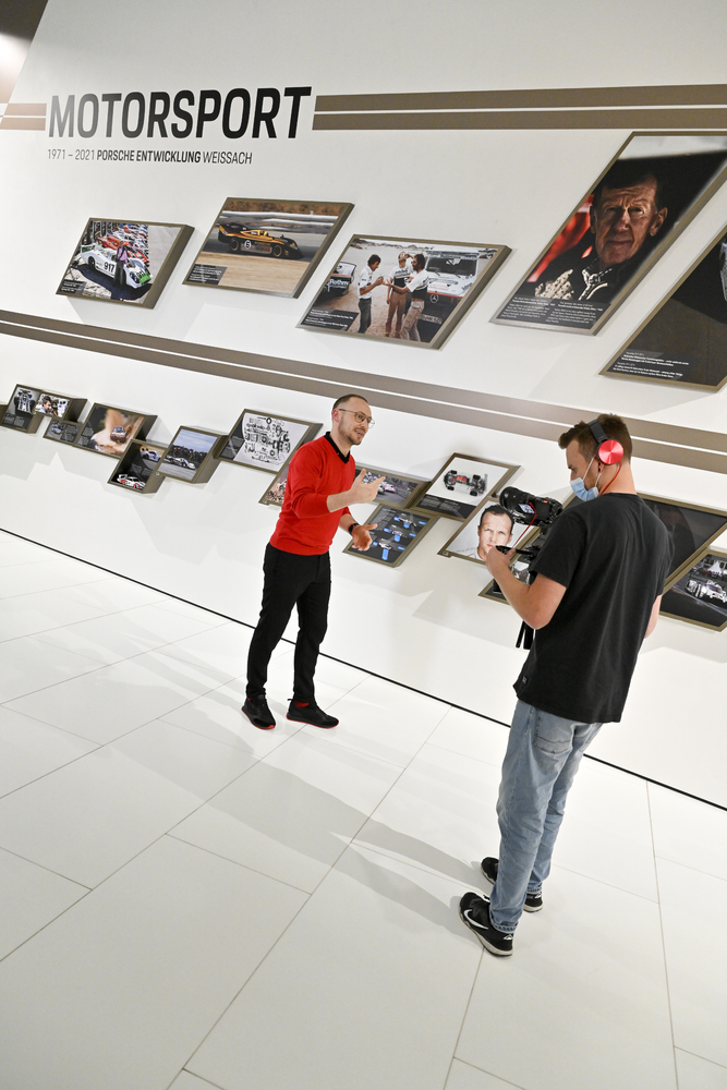 Wycieczka online do Porsche Museum - mężczyzna nagrywa drugiego mężczyznę w muzeum. 
