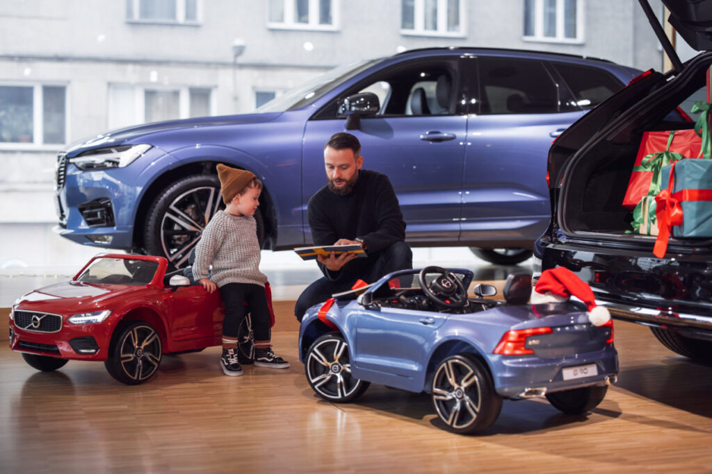 Volvo Car Poland kupi autka elektryczne dla dzieci w szpitalach - mężczyzna i chłopczyk siedzą na parkiecie przy dużych i małych samochodach. 