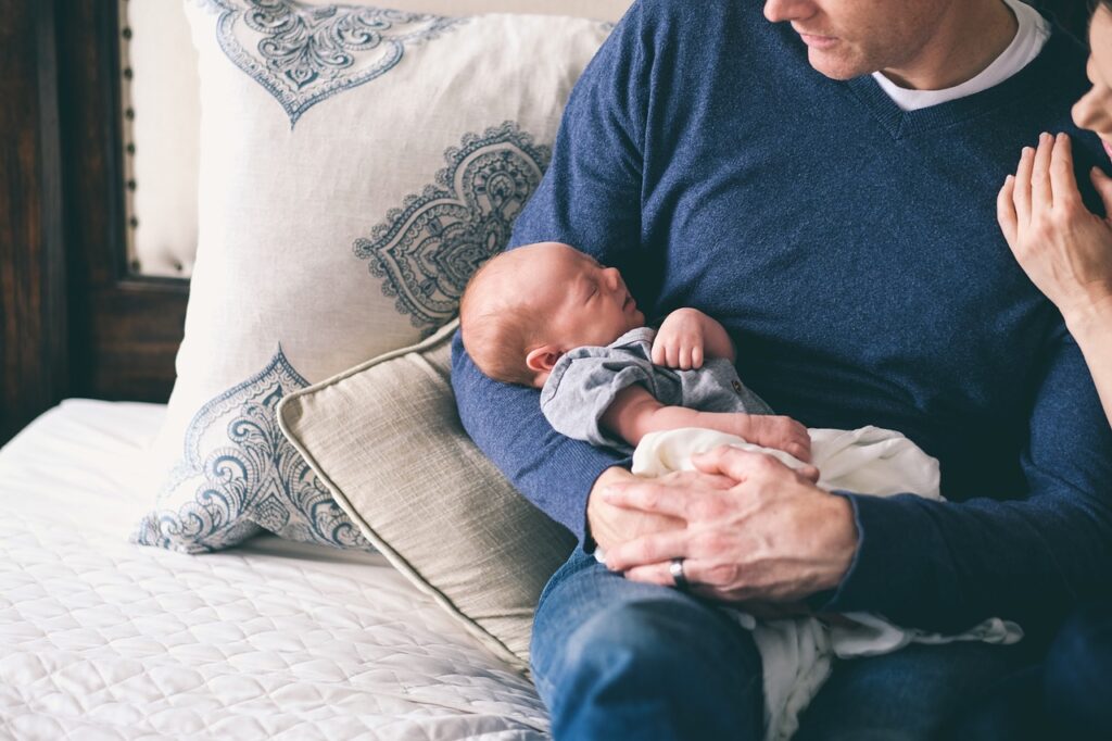 Zmiany w urlopach rodzicielskich - nowe przepisy już od 2022 roku mężczyzna siedzi na kanapie i trzyma w rękach noworodka. 