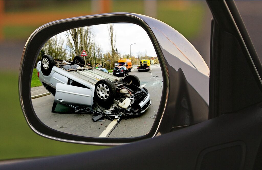 Aktualne stawki mandatów dla piratów drogowych - przewrócony samochód po wypadku lezy n jezdni, widziany w odbiciu w lustrze.