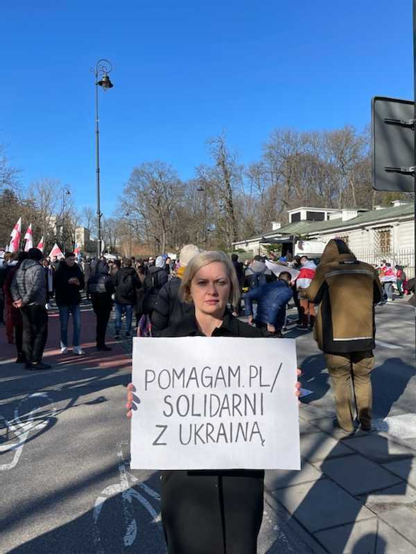 Pomagam.pl uruchamia zweryfikowane zbiórki “Solidarni z Ukrainą” dla firm - kobieta trzyma w dłoniach białą kartkę z czarnym napisem.