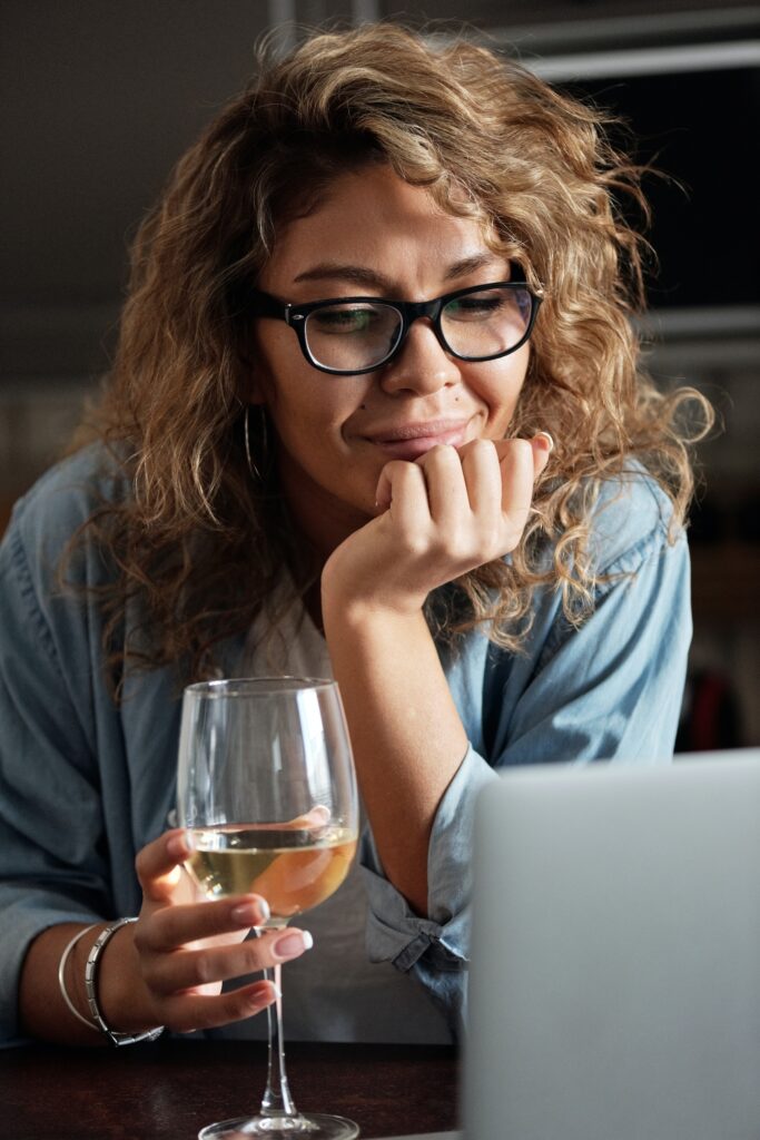 Kontrola trzeźwości pracowników budzi wątpliwości - kobieta  kieliszkiem wina siedzi przed otwartym laptopem.