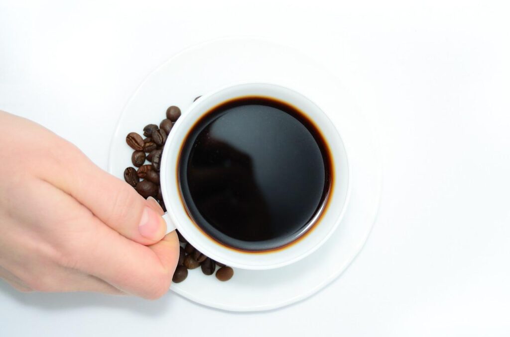Który ekspres wybrać: na kapsułki czy kolbowy? - dłoń trzyma filiżankę kawy.