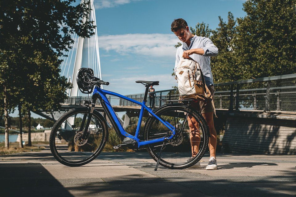 Polacy chcą rowerów elektrycznych z dofinansowaniem - mężczyzna stoi przy rowerze w tle most i rzeka.