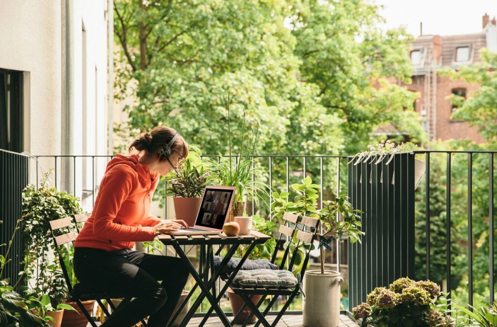 Workation – nowy trend pracy czy sposób na ucieczkę od służbowych obowiązków? - kobieta pracuje przed komputerem na balkonie wśród zieleni. 