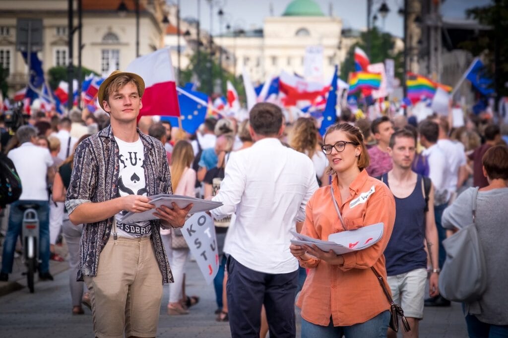 Patriotyzm przyszłości w rękach młodych - kobieta i mężczyzna trzymają plakaty w rękach na tle tłumu. 