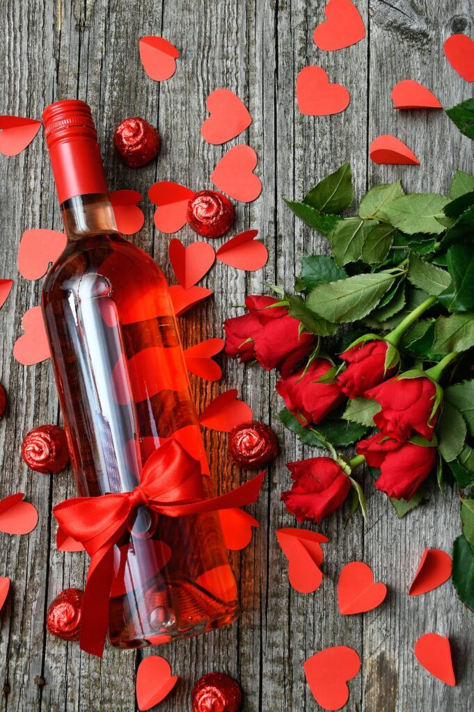 Kto i ile zarobi w Walentynki? - butelka wina, kwiaty i czerwone sedruszka leżą na stole. 